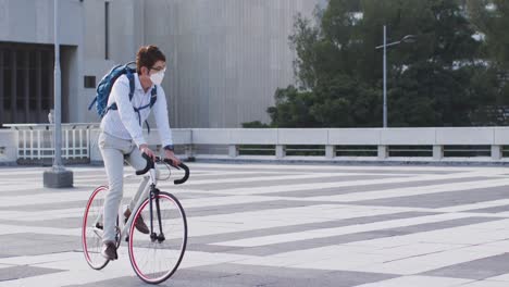 Hombre-Asiático-Con-Mascarilla-Montando-Bicicleta-En-El-Techo-Del-Parque-Corporativo