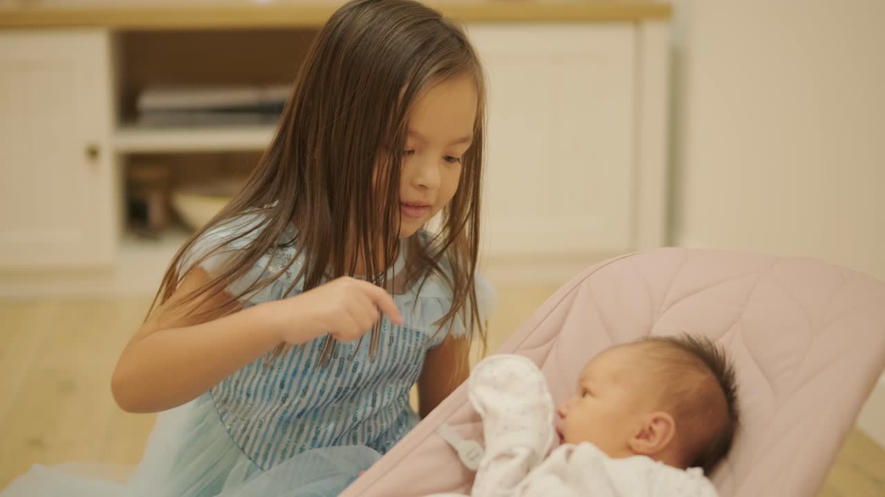 어린 소녀가 집에서 아기 여동생과 즐겁게 놀고 있습니다. 이 순간은 편안한 실내 환경에서 형제자매의 유대감과 가족 사랑을 포착합니다.