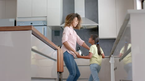 happy biracial mother and daughter having fun dancing together in kitchen, copy space, slow motion