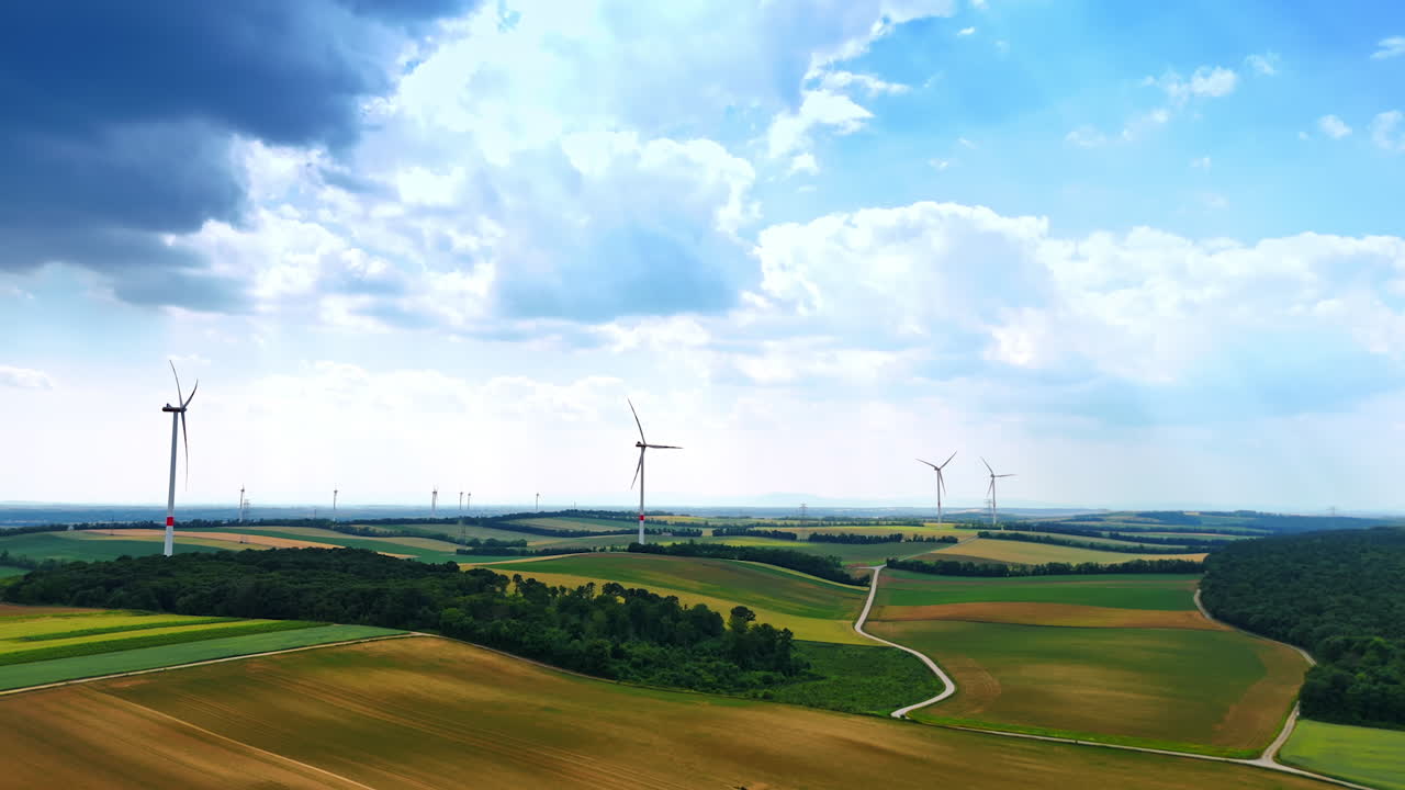 Large clouds gathered in the sky over the vast agricultural fields. Multiple wind mills rotate slowly producing renewable energy