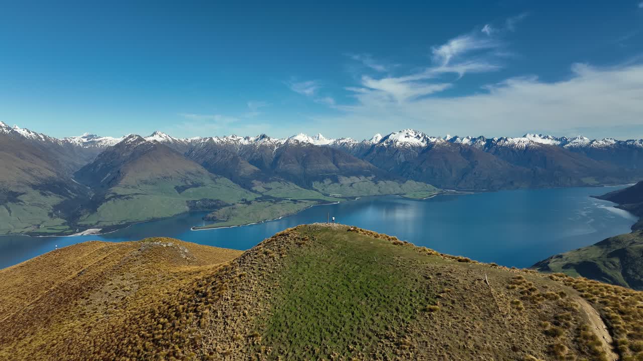 hombre de pie junto al poste de la cumbre de madera en el pico del istmo con vistas a los alpes del sur