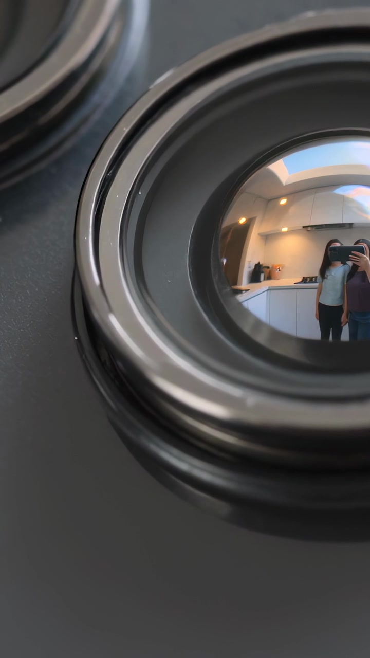 Video verticale: Inquadratura di un fornello che riflette una coppia in cucina mentre alza uno smartphone, con colori bianco e bordeaux.