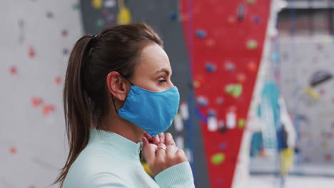 retrato de una mujer caucásica sonriente ajustando una máscara facial en un gimnasio de escalada cubierto