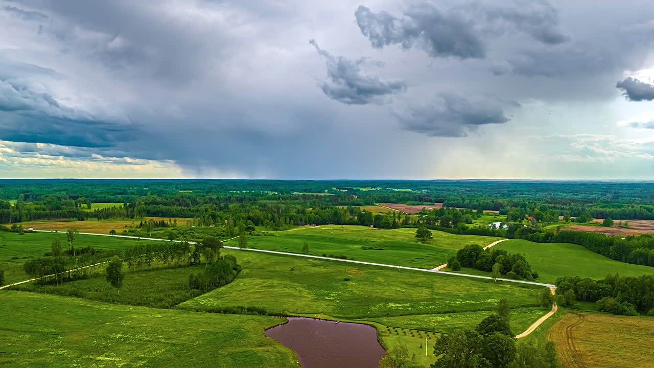 Cloudscape motion time lapse over farmland fields, village, and forest during summer in this dynamic aerial hyper lapse