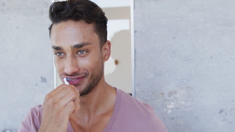 Happy-biracial-man-brushing-teeth-in-sunny-bathroom-in-the-morning,-slow-motion