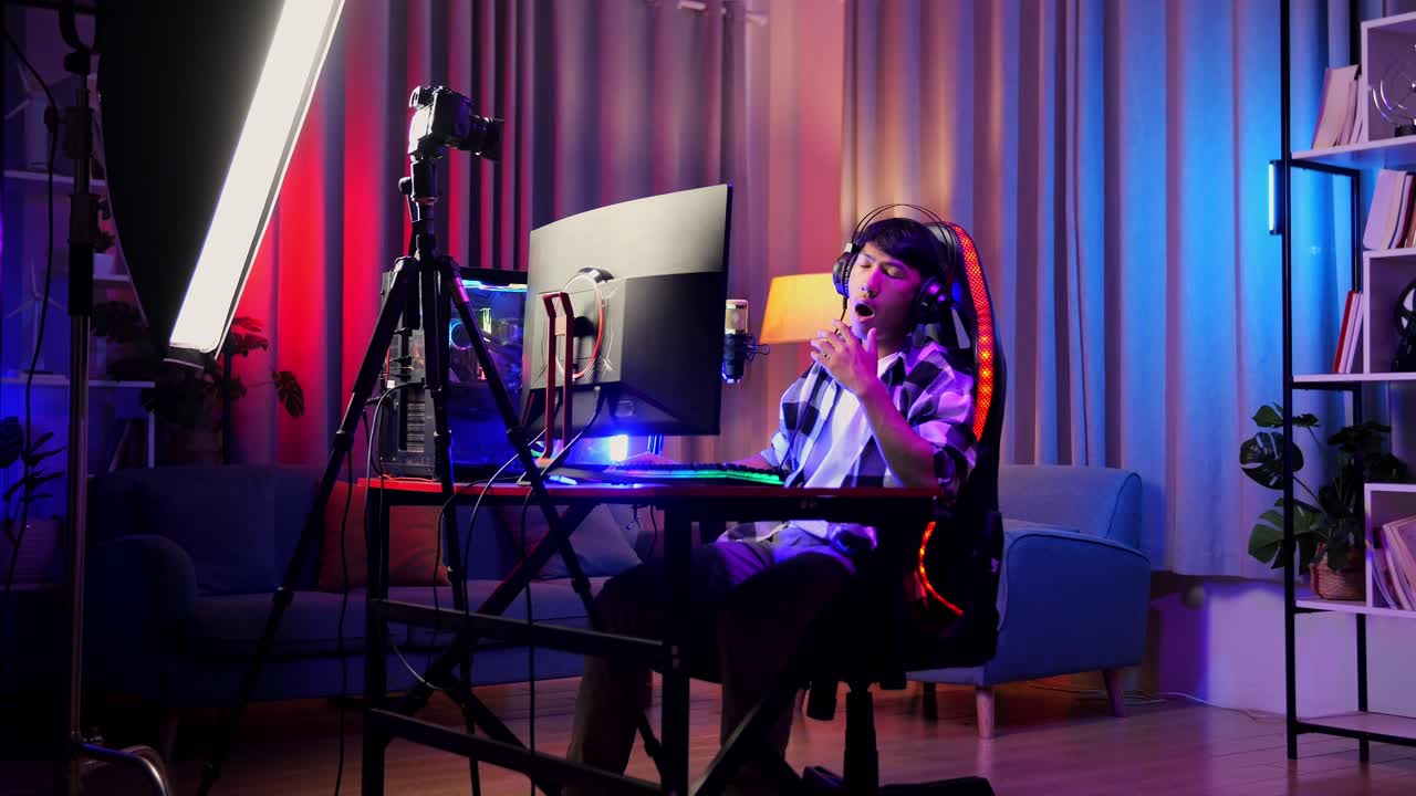 asian boy streamer jugando a un juego a través de la red en una computadora personal. bostezando y durmiendo, videojuego de transmisión en vivo, escritorio iluminado por luz de tira led rgb