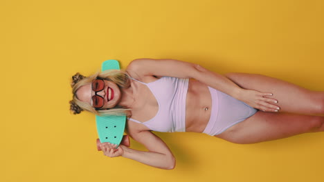 woman in bikini with skateboard on yellow background