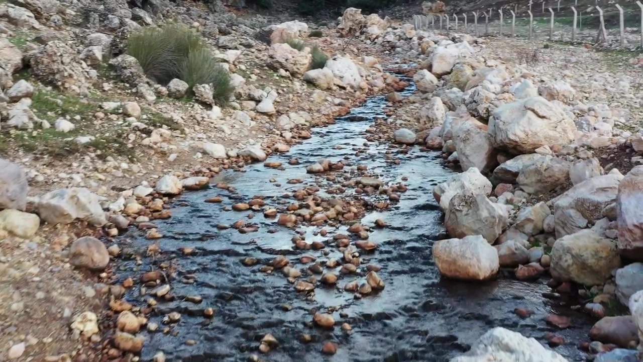 Clear stream flowing through rocky terrain in the Moroccan countryside with natural textures and peaceful mountain scenery. Ideal for nature and documentary projects.