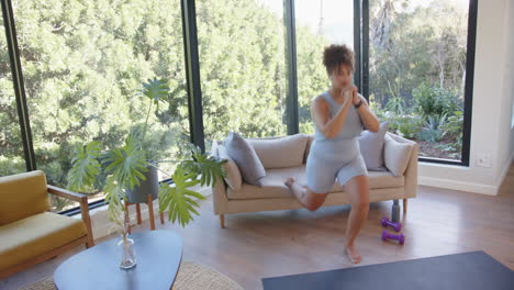 exercising at home, plus size woman doing lunges near sofa and dumbbells