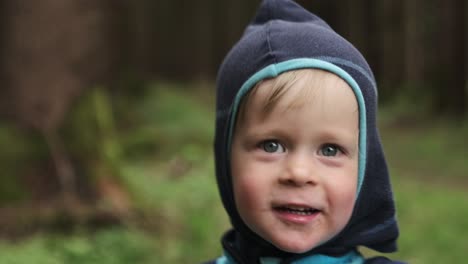 young boy turning towards the camera and laughing while in the forest