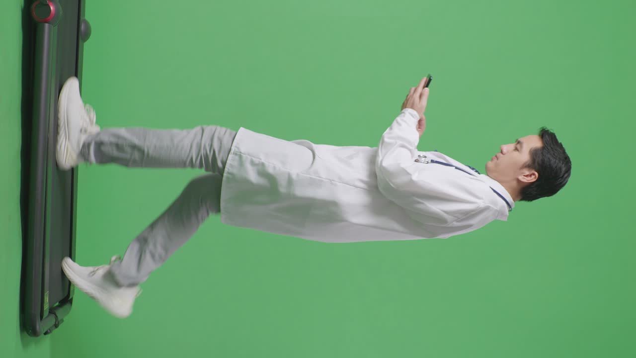 병원에서 녹색 화면 배경에서 는 동안 스마트폰을 사용하여 스테토스코프를 가진 아시아 남성 의사