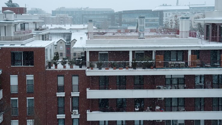 Idilliaca scena invernale con neve che cade intorno a un edificio residenziale. La luce soffusa, l'ambiente tranquillo e la nevicata costante creano un'atmosfera calma e cinematografica con un'atmosfera stagionale pacifica.