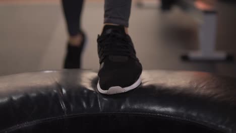 Close-up-footage-of-fitness-girl-feet.-Girl-in-black-leggings-and-sneakers-rises-on-a-high-stand-changing-legs,-doing-cardio-in-gym.-Slow-motion