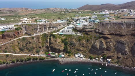 Aerial-flying-towards-Greek-Islands,-rocky-cliff-and-villas-on-beach-in-Santorini,-Greece