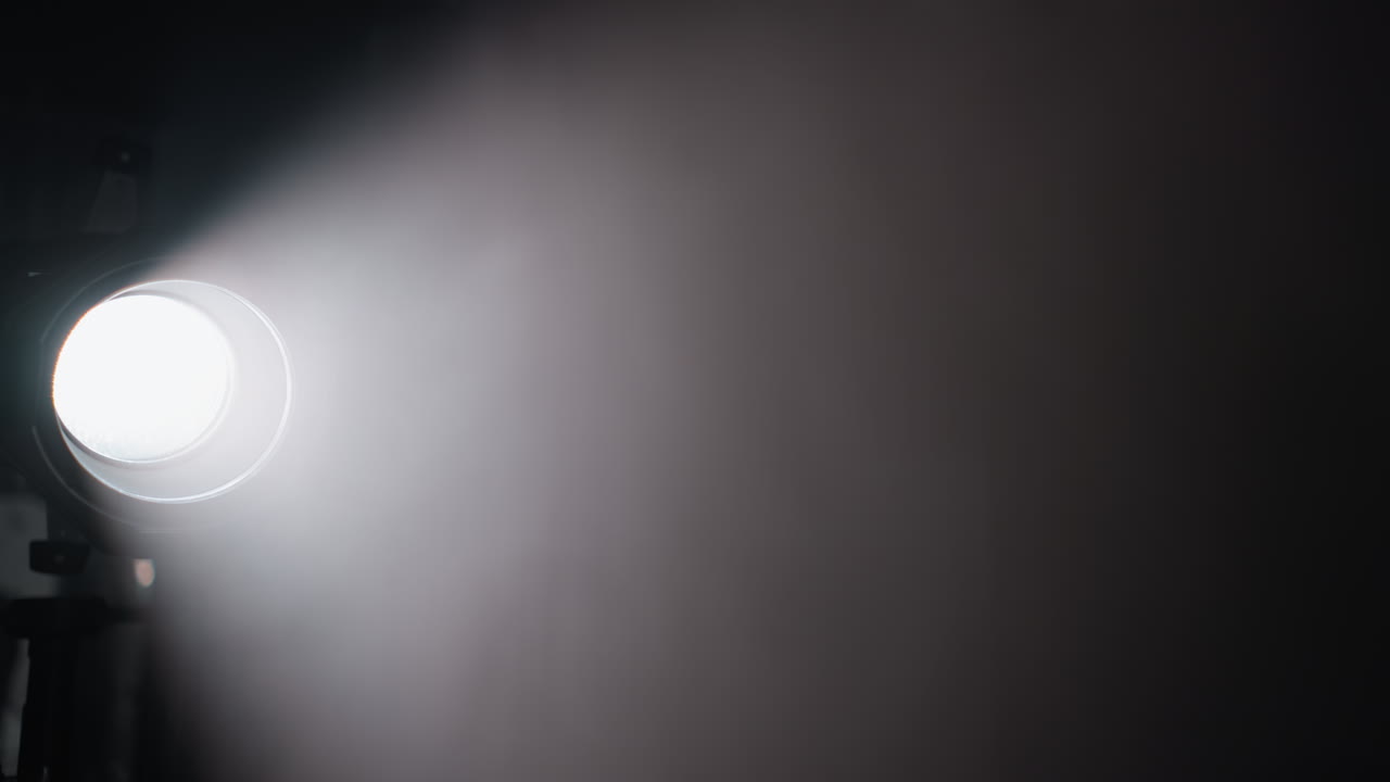reflector de estudio proyectando un fuerte haz de luz a través de una habitación oscura, destacando el humo y la atmósfera