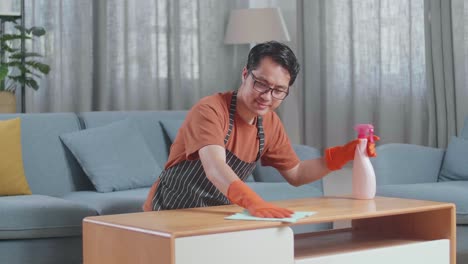 집에서 스프레이로 테이블을 청소하는 아프론을 입은 아시아 남성 집주인