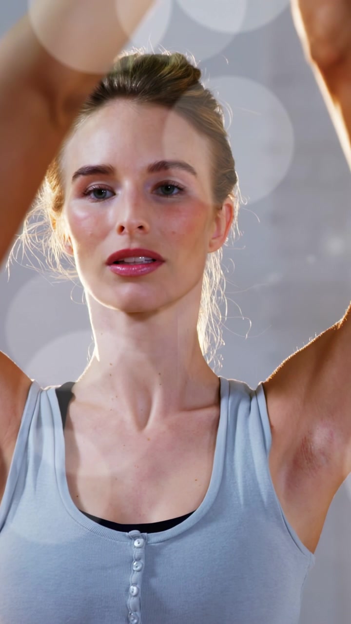 Dikey video: Kadın nefes alıyor ve fitness yaparken kollarını yüzünün önünde kavuşturuyor, odaklanmak için bokeh efektiyle gizleniyor.