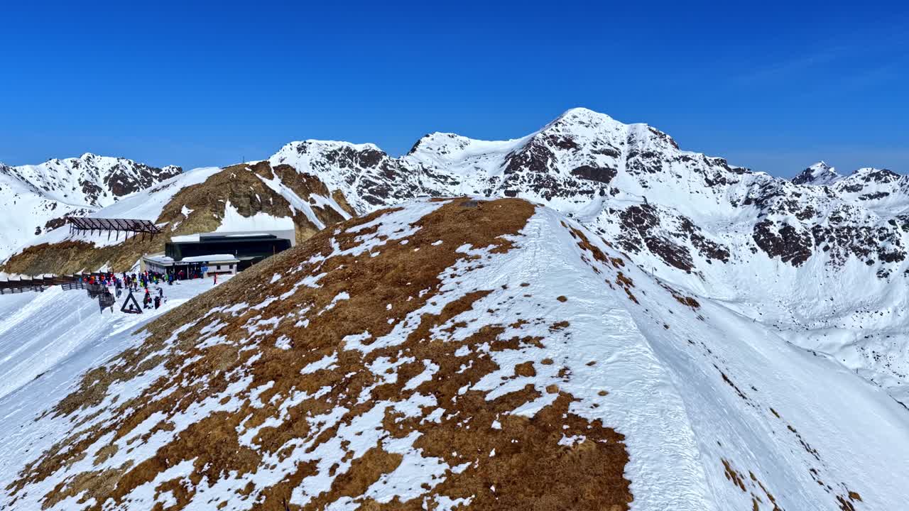 Veduta aerea di una stazione a monte di un impianto di risalita su una stretta cresta innevata con sciatori in coda e linee di cabinovie. Serfaus Fiss Ladis, Austria