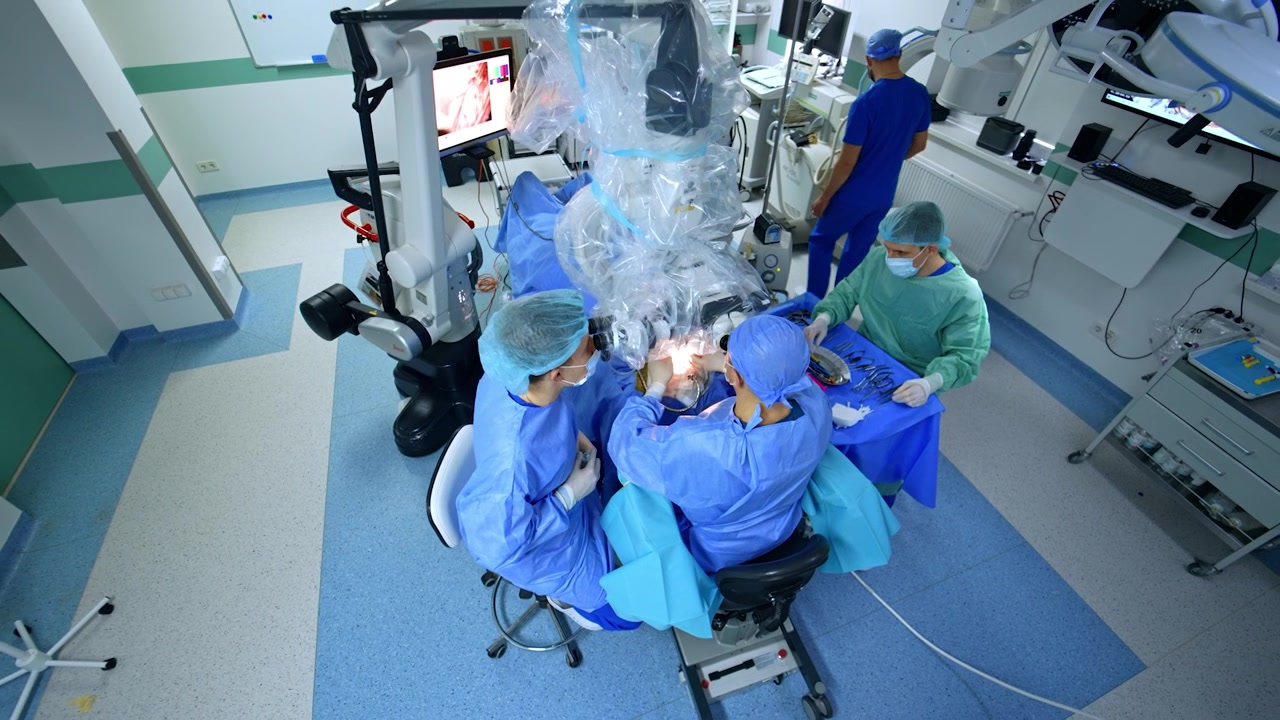 Operational field in the modern surgical room. High angle view. Doctors sit at microscope performing surgery.