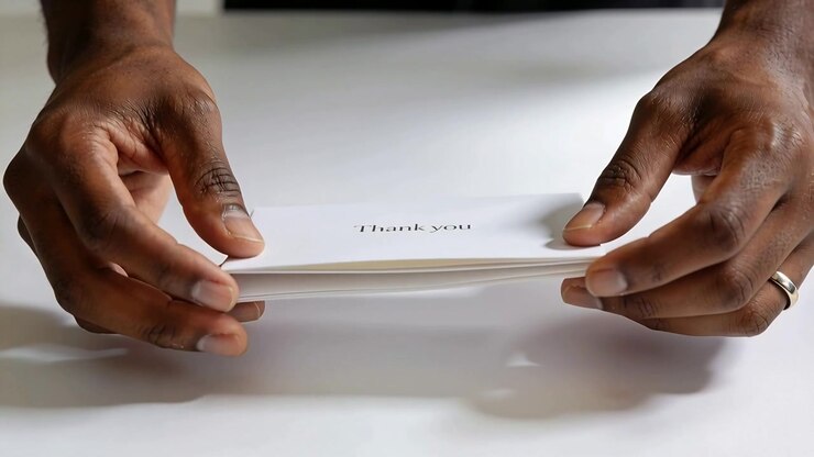Reaching hands opening folded thank you card on white table, revealing interior, dark top, ring