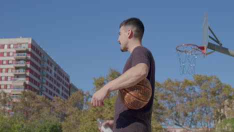 Medium-shot-of-a-young-Caucasian-man-drinking-an-isotonic-drink-in-the-break-from-playing-on-a-city-street-basketball-court-on-a-sunny-day