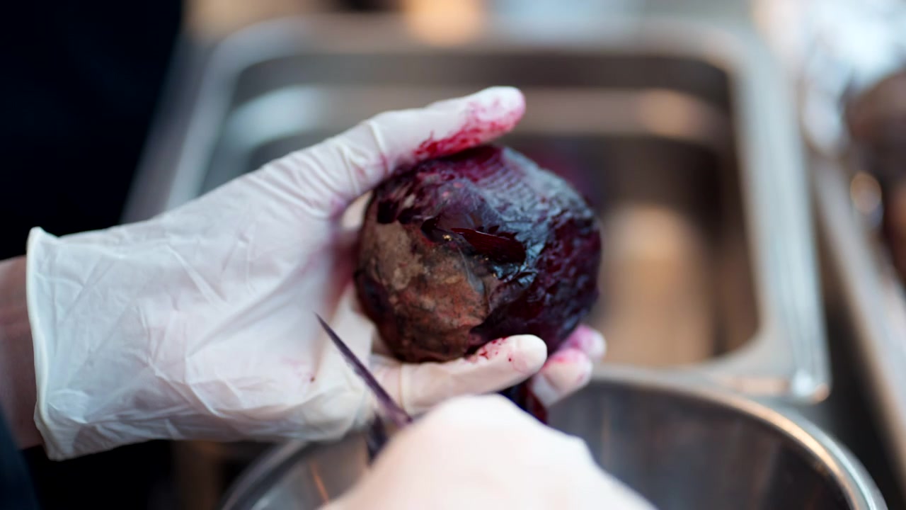 Closeup of Hand In Gloves Peeling Skin Of Beetroot.