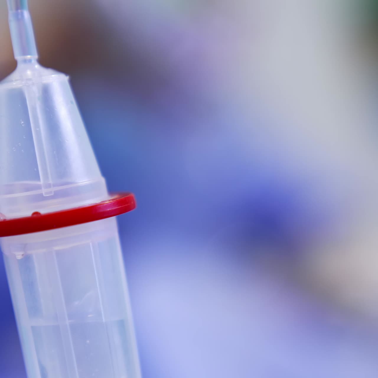 Reservoir of drop counter is filling with medicines. Saline solution dripping slowly close up. Blurred backdrop