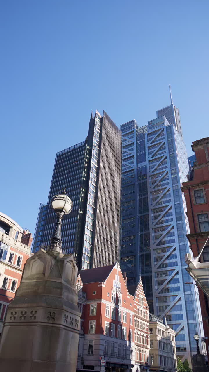 Modern glass skyscrapers of London's financial district reflecting the blue sky next to historic architecture. Vertical