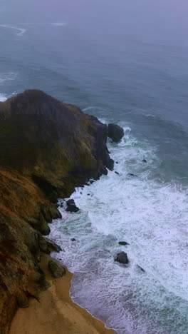 waves of ocean moving slowly to the rocks at the waterfront. montara state beach at california, united states. vertical video