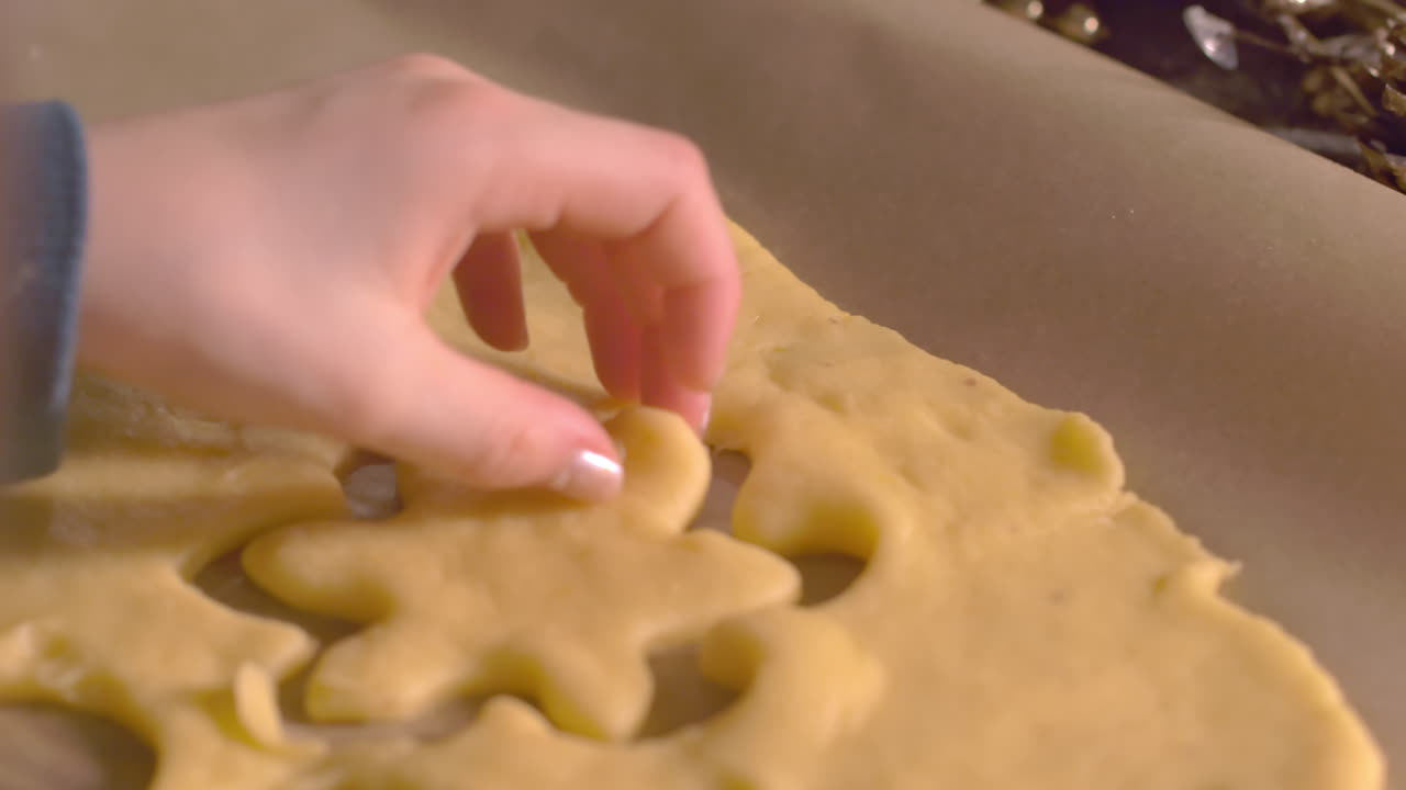 Girl hand pressing snow flake shape cookie cutter in fresh dough on baking sheet