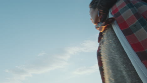 young woman walking on grassy lake shore at sunset, looking up at sky