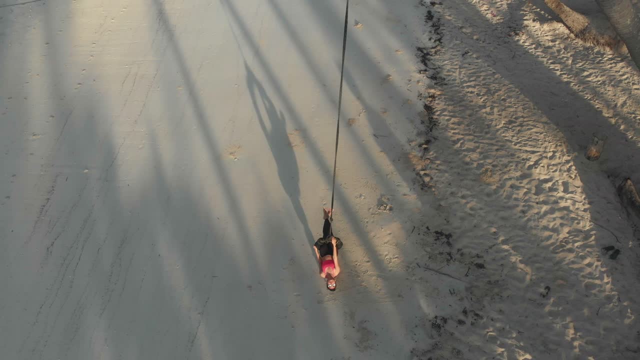 Aerial view of woman on rope swing overlooking boat at beautiful sunrise Paliton Beach Siquijor Philippines