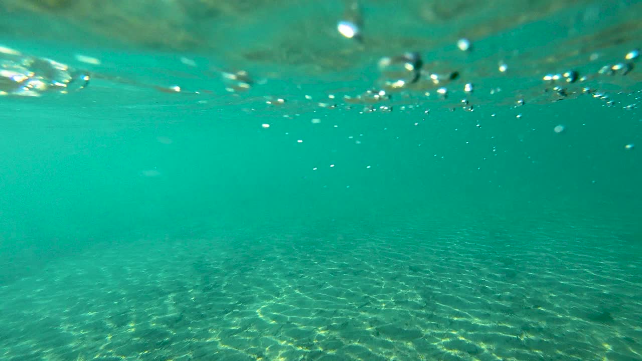 Turquoise underwater texture with air bubbles and sunlight reflecting on river bottom, copy space