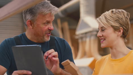 female apprentice learning from mature male carpenter with digital tablet in furniture workshop