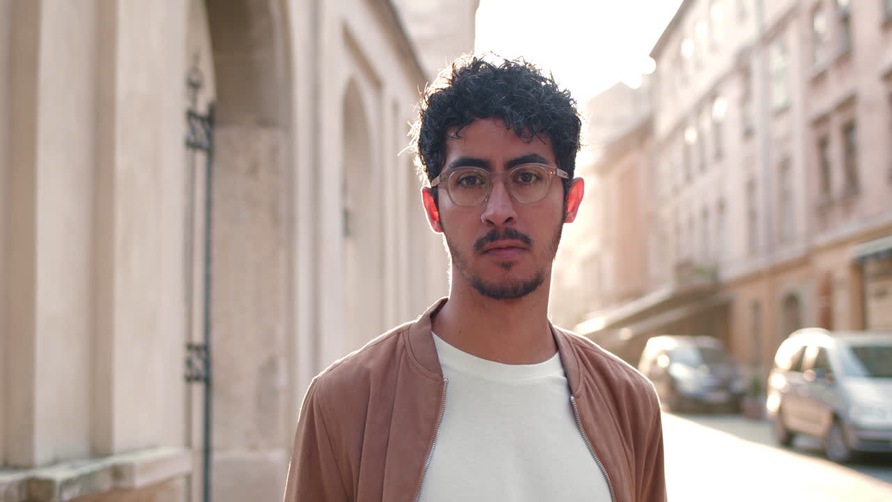 Portrait of a man with curly hair and glasses in an urban setting