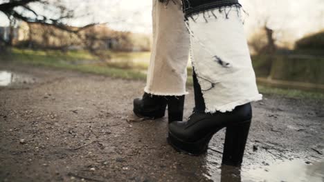 young woman in a black coat walking across a puddle in a park in autumn in afternoon