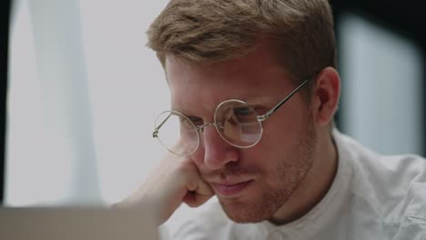 hombre caucásico inteligente con gafas está leyendo información en la pantalla de la computadora portátil, vista de cerca de la cara