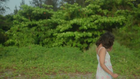 una mujer joven en un vestido floral se aleja en un camino de arena, vegetación exuberante en el fondo