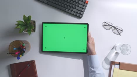 vista de arriba hacia abajo de una computadora portátil con pantalla verde simulada pantalla chromakey en un escritorio de oficina de madera al lado de la libreta con bolígrafos, gafas y un vaso de agua.