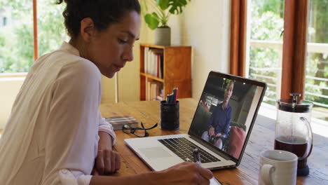 african american woman taking notes while having a video call on laptop at home