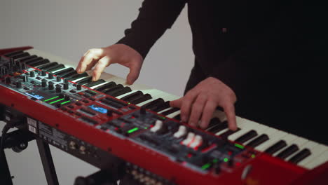 close view of a hand playing a red sampler piano against a plain white background, highlighting the focus on the instrument and the musicians fingers in motion