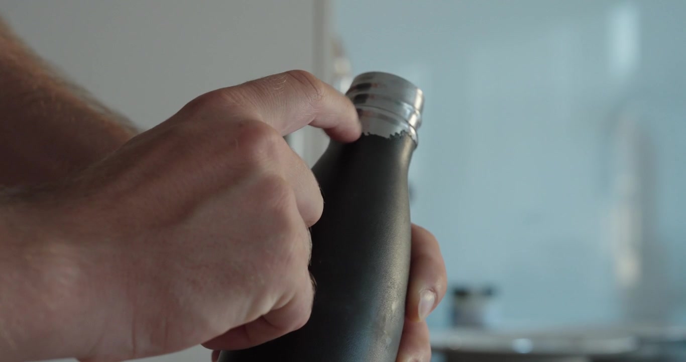 Close-up of a hand pointing at chipped and peeling paint on a metal thermos bottle, showing surface wear and damage.
