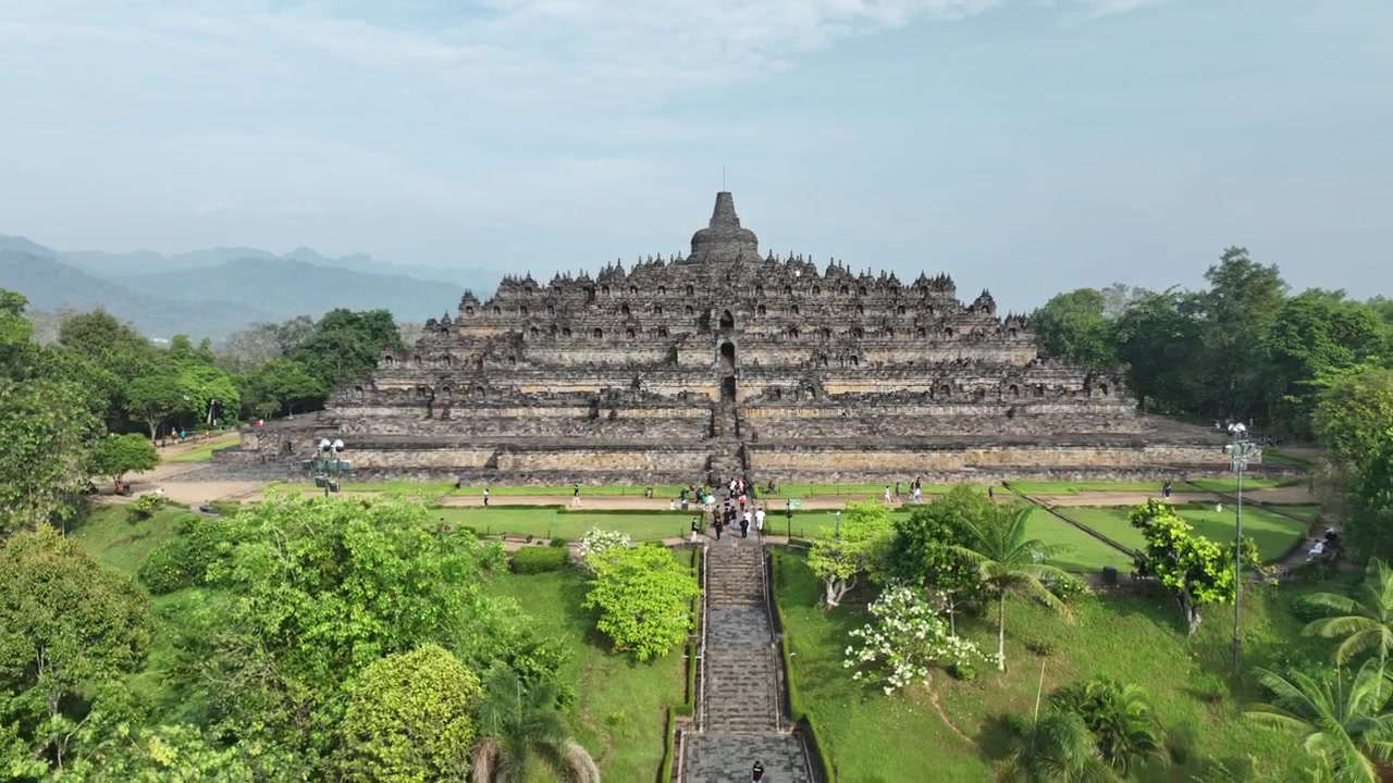 Riprese aeree del Tempio di Borobudur a Giava Centrale, Indonesia, che mostrano le sue dettagliate sculture in pietra, grandi stupa e il paesaggio verde lussureggiante che circonda questo sito Patrimonio dell'Umanità UNESCO.