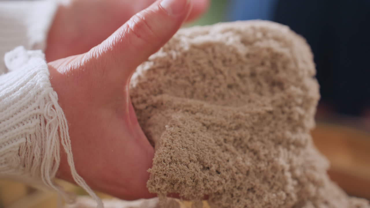Close up view of guest lifting soft soil mold with both hands in gentle motion during therapeutic session, capturing mindful sensory engagement and calming indoor environment with natural light