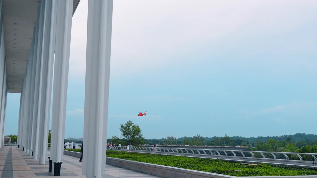 Washington, USA, 13 giugno 2026: Colonnato della terrazza del Kennedy Center con elicottero rosso sopra il fiume Potomac. Colonne di marmo bianco incorniciano un giardino pensile verde, il fiume e la lontana linea degli alberi della Virginia