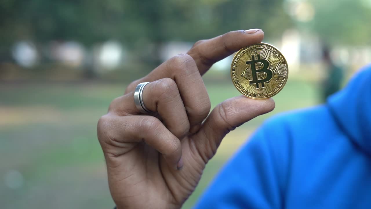 toma de una mano asiática sosteniendo una moneda de bitcoin de criptomoneda al aire libre en el fondo del parque