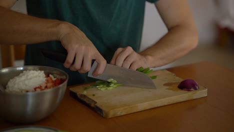 Close-up-man-cutting-green-onion-on-wooden-board,-filmed-in-slow-motion