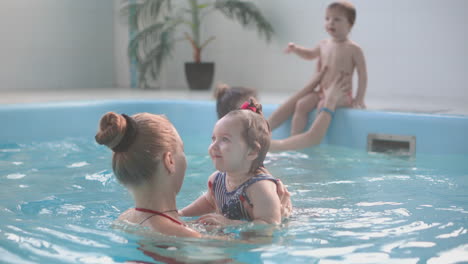 Happy-middle-aged-mother-swimming-with-cute-adorable-baby-in-swimming-pool.-Smiling-mom-and-little-child,-newborn-girl-having-fun-together.-Active-family-spending-leisure-and-time-in-spa-hotel.