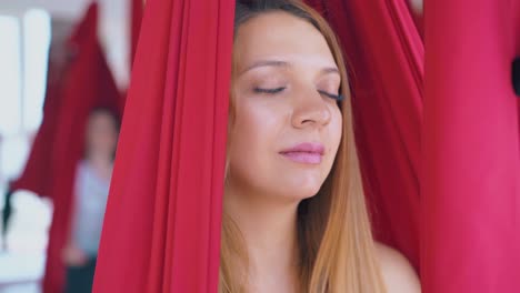 relaxed lady sits with closed eyes in fly yoga hammock