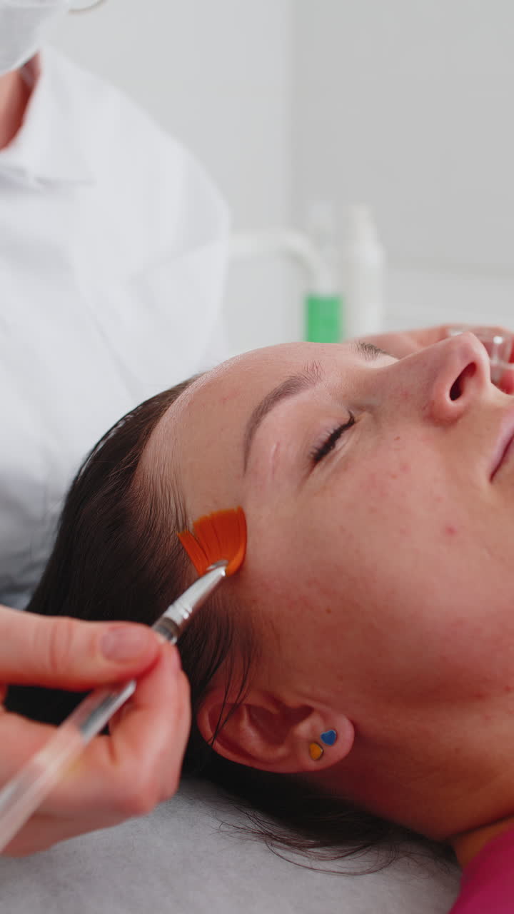 terapia enzimática esteticista aplicando crema médica hidratante en la cara de una mujer joven adulta con pinceles